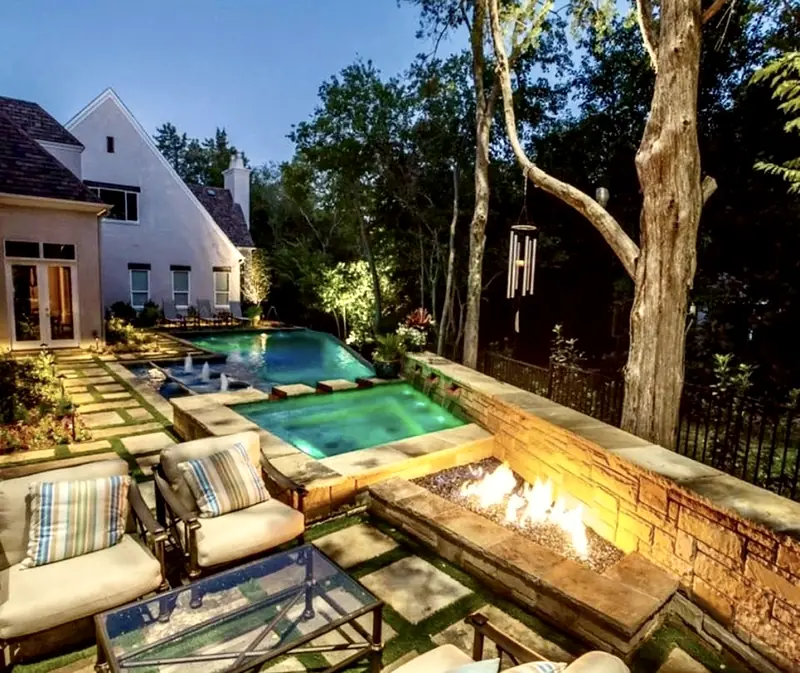 The same yard at dusk: the spa lit up, bubblers on the shelf, and the linear fire pit burning