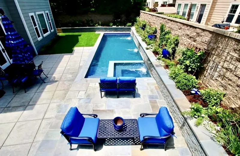 Lap pool and spa with a fire table and blue lounge chairs on the deck