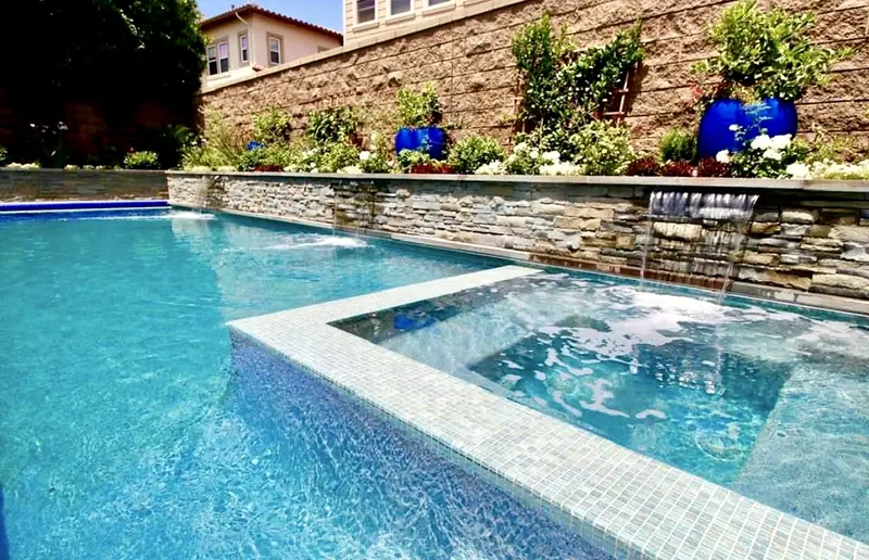 Tiled spa set into a long lap pool, with a stacked-stone wall and planters behind