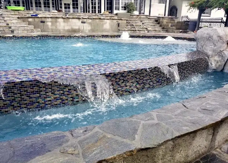 Raised spillway wall with glass tile and sheer descents into the pool
