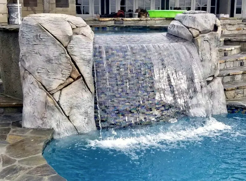 Rock-framed waterfall pouring over an iridescent glass-tile wall
