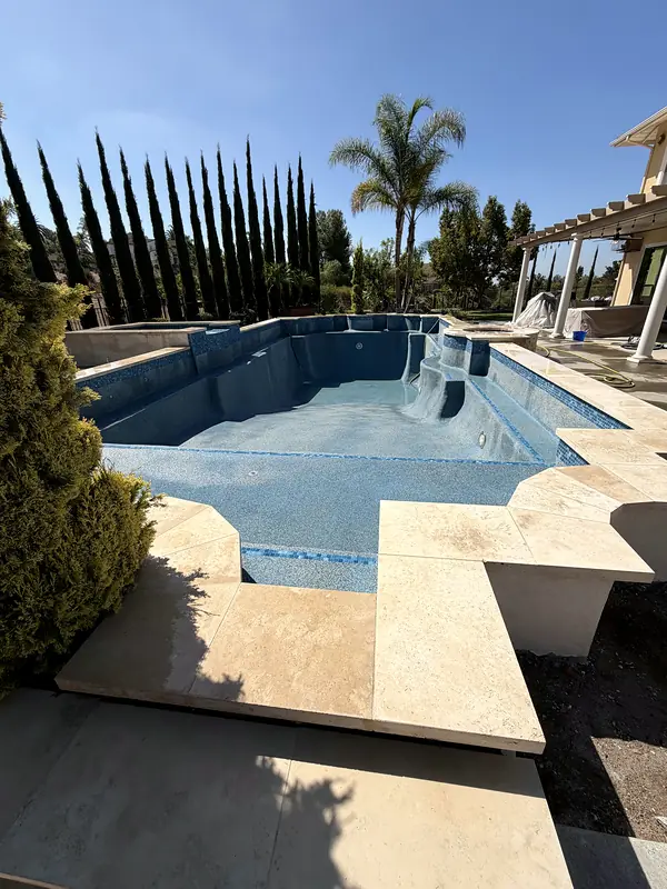 Travertine coping along the remodeled pool, with a row of cypress and palms behind