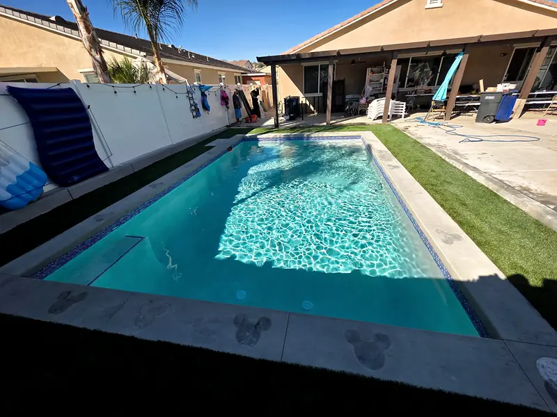Rectangular pool with a glass-tile waterline and artificial turf running to the fence